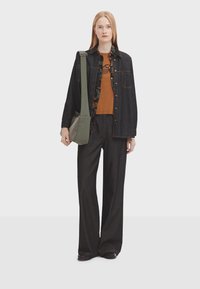 Denim shirt jacket with button closure, paired with a brown t-shirt. Black wide-leg trousers and a green crossbody bag complete the outfit.