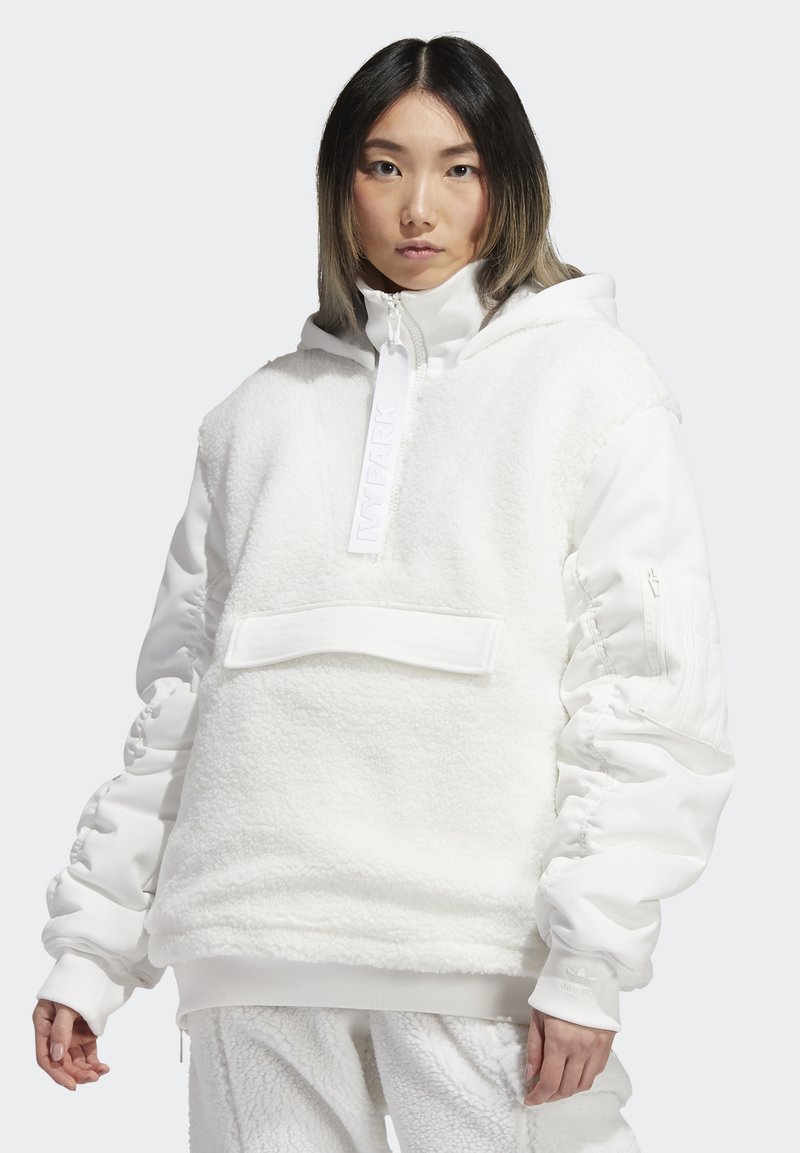 Biały polarowy sweter z zamkiem błyskawicznym na szyi, kapturem i kieszenią typu pouch. Posiada ściągacze na mankietach i teksturowany materiał. Gładkie akcenty na rękawach.