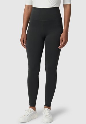 Hoge zwarte legging van rekbaar materiaal, met een naadloos ontwerp en een aansluitende pasvorm, gecombineerd met witte sneakers.