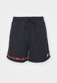 Svarta Nike träningsshorts med elastisk midja, dragsko, orange "Nike Athletics"-text längs nederkanten och vitt Nike swoosh-logotyp på benet.