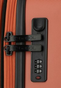 Detalle de una maleta naranja de carcasa dura que presenta tiradores de cremallera negros, un candado de combinación con tres diales y una superficie texturizada para un mejor agarre.