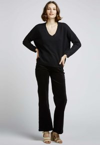 Pull noir à col V, coupe décontractée ; associé à un pantalon noir évasé et des sandales à talons beiges. Texture douce, design minimaliste, sans motifs.