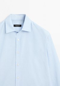 Jasnoniebieska męska koszula wizytowa z cienkimi białymi pionowymi paskami i białymi guzikami, z klasycznym kołnierzykiem i metką marki wewnątrz.