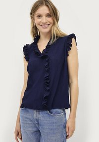 Navyblauw mouwloos shirt met een gerimpelde v-hals, textuurstof en een relaxte fit, gecombineerd met lichtblauwe denimjeans.