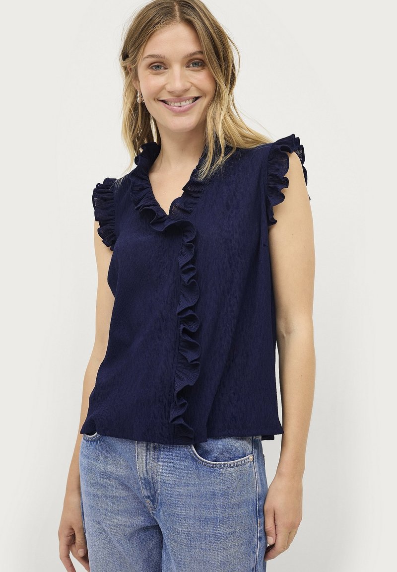 Navyblauw mouwloos shirt met een gerimpelde v-hals, textuurstof en een relaxte fit, gecombineerd met lichtblauwe denimjeans.