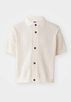 Short-sleeve cream cardigan with a button-down front, featuring vertical knit patterns and brown buttons on a ribbed hem and collar.