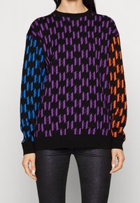 Felpa colorata con una base nera e un motivo geometrico in viola, blu e arancione. Maniche lunghe e polsini a coste.