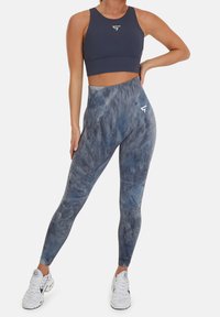 Blå batikleggings med hög midja, texturerad tyg och logotypdetalj, i kombination med en matchande blå sportbh. Vita sneakers fulländar looken.