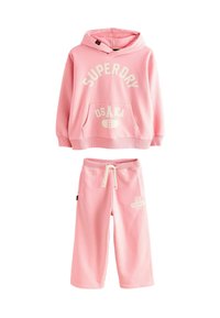 Haut à capuche rose pour enfants avec le texte "SUPERDRY OSAKA 6" et un pantalon de jogging rose assorti avec l'imprimé "23 SUPER DRY" sur la jambe gauche.