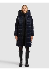 Mornarsko plava prešivena jakna s kapuljačom, patentnim zatvaračem i bočnim džepovima. Uparen s crnim čizmama do koljena.