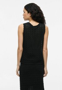 Top sin mangas de punto negro con un escote ondulado y un patrón en zigzag. Tejido texturizado con dobladillo ajustado y diseño estructurado.