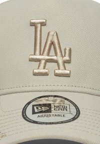 Justerbar beige cap med et broderet LA-logo i lys beige. Inkluderer et rundt New Era-mærke på undersiden af skyggen.