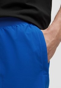 Ljust blå shorts med en texturerad tyg, elastiskt midjeband och sidofickdetalj, delvis täckta av en svart skjorta.