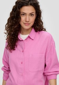Roze overhemd met knopen, gemaakt van textuurstoffen, met een zak op de linkerborst en opgerolde mouwen.