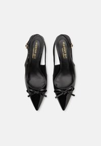 Svarta lackskin slingback-klackar med spetsiga tår, rosetter framme och guldtryck på inläggen.