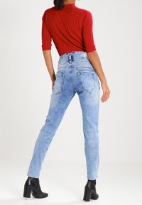 Světlé modré džíny s vysokým pasem a slim fit, zadní kapsy a vybledlý vzhled. Zkombinováno s červeným žebrovaným topem a černými kotníkovými botami na podpatku.