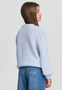 Jasnoniebieski sweter z dzianiny z okrągłym dekoltem, balonowymi rękawami i ściągaczami. W połączeniu z dżinsami o wysokim stanie.