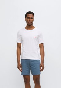 White short-sleeve T-shirt with a crew neck and red "HUGO" logo, paired with blue textured shorts. Simple and casual design.