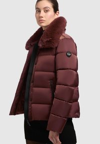 Burgundská prešívaná bunda s umelým kožúškom na golieri, prešívaným dizajnom, bočnými vreckami na zips a logom na rukáve. Sofistikovaný, lesklý materiál.