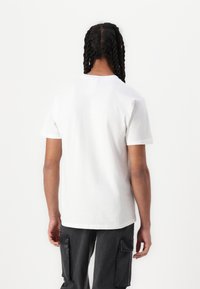 Hvid bomulds t-shirt med korte ærmer, rund hals, afslappet pasform og glat tekstur. Bæres med mørke cargobukser med sidelommer.