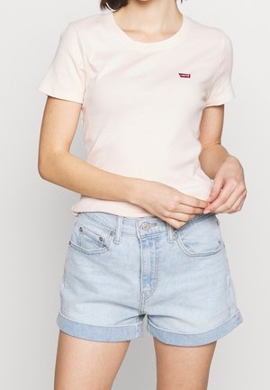 Hellrosa Baumwoll-T-Shirt mit kurzen Ärmeln, rundem Ausschnitt und einem kleinen roten Levi's-Logo-Patch auf der linken Brust, kombiniert mit hellblauen Denim-Shorts.
