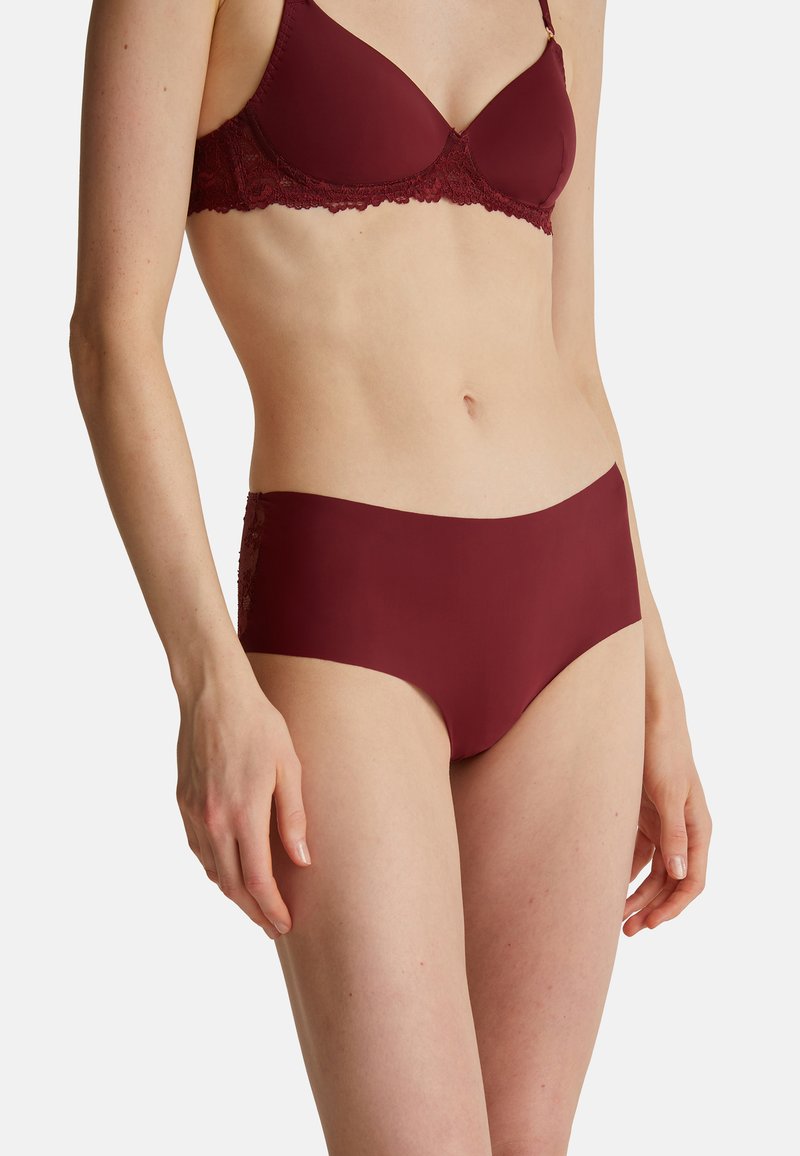 Burgundský souprava spodního prádla obsahující podprsenku s krajkovými akcenty a odpovídající kalhotky, vyrobená z hladkého materiálu s bezproblémovými okraji, což zajišťuje elegantní vzhled.