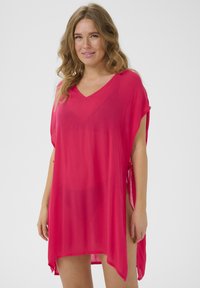 Funda de playa vibrante en color rosa, hecha de un tejido ligero y transparente. Presenta un escote en V, mangas cortas y acentos de lazo en los laterales para un ajuste ajustable.