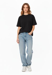T-shirt nera a maniche corte abbinata a jeans dritti blu chiaro e sneakers bianche. Il tessuto è morbido e ha una vestibilità rilassata.