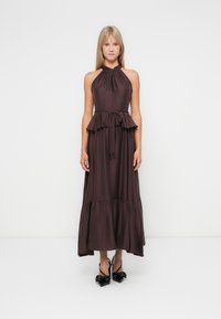 Lila Halftermaxikleid mit gerafftem Oberteil, Peplum-Taille und schichtigem Rock. Kombiniert mit schwarzen, schuhen mit Schleifenakzent.