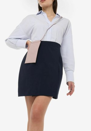 Marineblå nederdel med lige snit, parret med en lys blå stribet oversized skjorte. En lille lyserød crossbody-pung hænger fra skjorten.