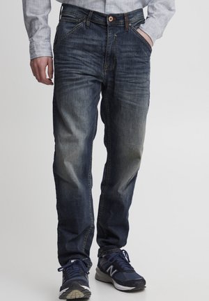 Blå denim jeans med rett ben design, med falming på lårene, fem lommer og knappelukking. Kombinert med mørke sneakers.