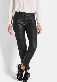 Pantalons en cuir noir au toucher lisse, avec une coupe ajustée, des coutures verticales et une taille mi-haute, associés à des baskets noires.