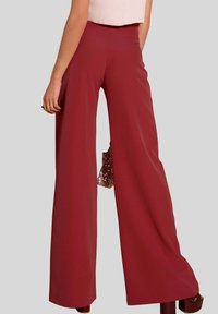Pantalones de pierna ancha en un rojo profundo, de tela suave. Cintura alta con bolsillos laterales y detalles en el dobladillo. Livianos, con una silueta fluida.