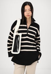 Black and cream striped pullover with a zippered collar, made of knit fabric. Accented by a black and white fuzzy shoulder bag.