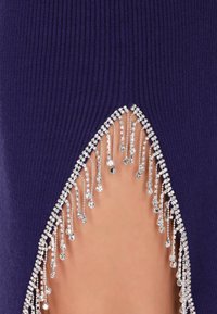 Robe violette côtelée avec une fente haute sur la cuisse ornée de strass argentés en cascade et de délicats accents en perles le long du bord.