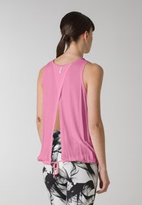 Pink ærmeløs top med en dyb udskæring på ryggen, samlet kant og snøredetalje. Glat tekstur med et let design.