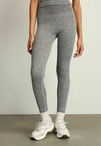 A szürke, bordázott leggings magas derekú, testhez simuló fazonú és texturált anyagú. Fehér sportcipővel és bokazoknival párosítva.
