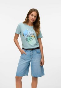 Lichtblauwe katoenen t-shirt met een lijntekening van twee gezichten, gecombineerd met lichte denim shorts en een bruine riem.