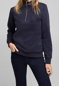 Mörkblå sweatshirt med hög krage, halv dragkedja och texturerad panel på bröstet. Tillverkad av mjukt tyg med ribbade ärmslutar och nederkant.