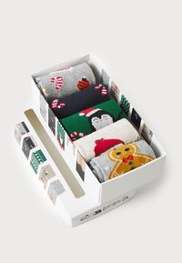Conjunto de quatro meias festivas numa caixa de presente. As características incluem cores cinza, verde, azul escuro e bege, com padrões de bengalas de doce, um pinguim e um homem de gengibre.