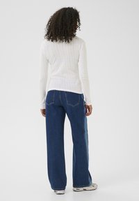 Vit ribbad långärmad topp tillsammans med högmidjade blå jeans, med detaljer i sidopaneler, avslutad med ljusa sneakers.