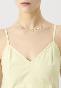 Collier en ton doré présentant des motifs floraux avec des accents rose et jaune, entrecoupés de perles blanches, sur une chaîne délicate.
