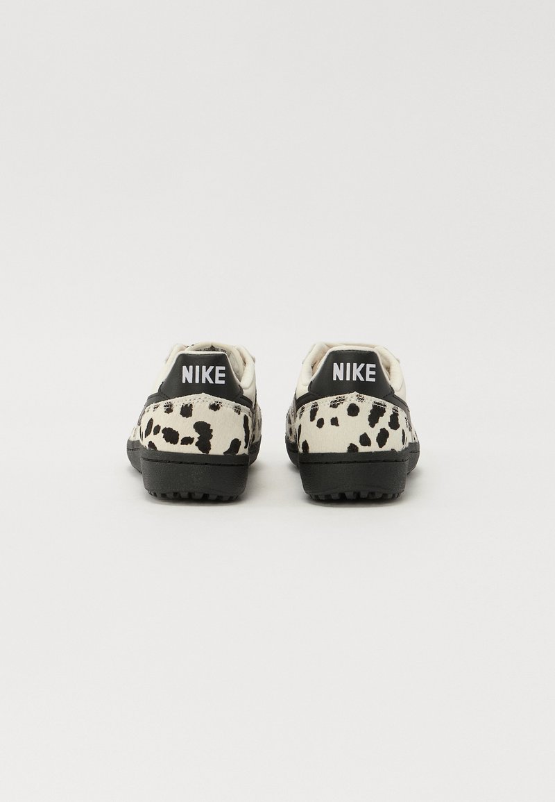 Baskets Nike avec une tige crème parsemée de taches noires, des accents noirs au talon et une semelle noire texturée. Logo affiché au niveau du talon.