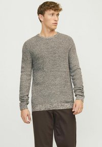 Gebreide trui in lichtgrijze en donkerbruine tinten, met een ronde hals en lange mouwen met ribgebreide manchetten, gecombineerd met donkere broek.