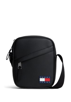 Kompakt sort crossbody taske med diagonalt lynlås og justerbar rem, med Tommy Jeans logo mærke i rød, hvid og blå.