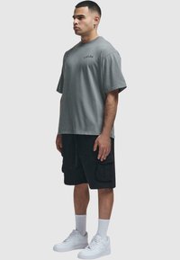 Grå bomull T-skjorte med avslappet passform, korte ermer og logo-detalj. Kombinert med svarte cargo-shorts og hvite joggesko.