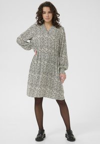 Rochie cu un model alb și negru, cu mâneci lungi, decolteu în V, talie strânsă și fustă evazată; purtată cu pantofi negri și colanți.