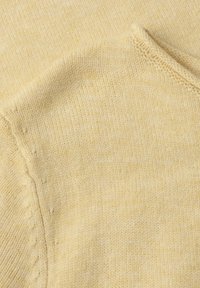 Gros plan d'un tissu tricoté doux beige montrant une couture détaillée et une texture subtile avec une couture traversant la surface en diagonale.