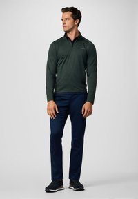Suéter de manga larga de color verde oscuro con cuello de cremallera de un cuarto, combinado con pantalones azul marino y zapatillas negras. Textura suave, ajuste casual.