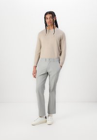 Lys beige langærmet sweater parret med lysegrå bukser. Skoene er hvide med sorte detaljer. Glat stof, tætsiddende pasform og minimal detaljer.